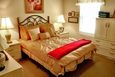 Beige bed in small bedroom with white side table and dresser